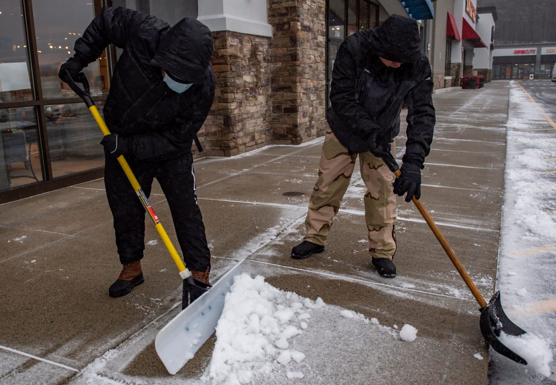 Workers clear snow and sleet from a shopping plaza sidewalk during a winter storm in Saugus. (Joseph Prezioso / AFP via Getty Images)