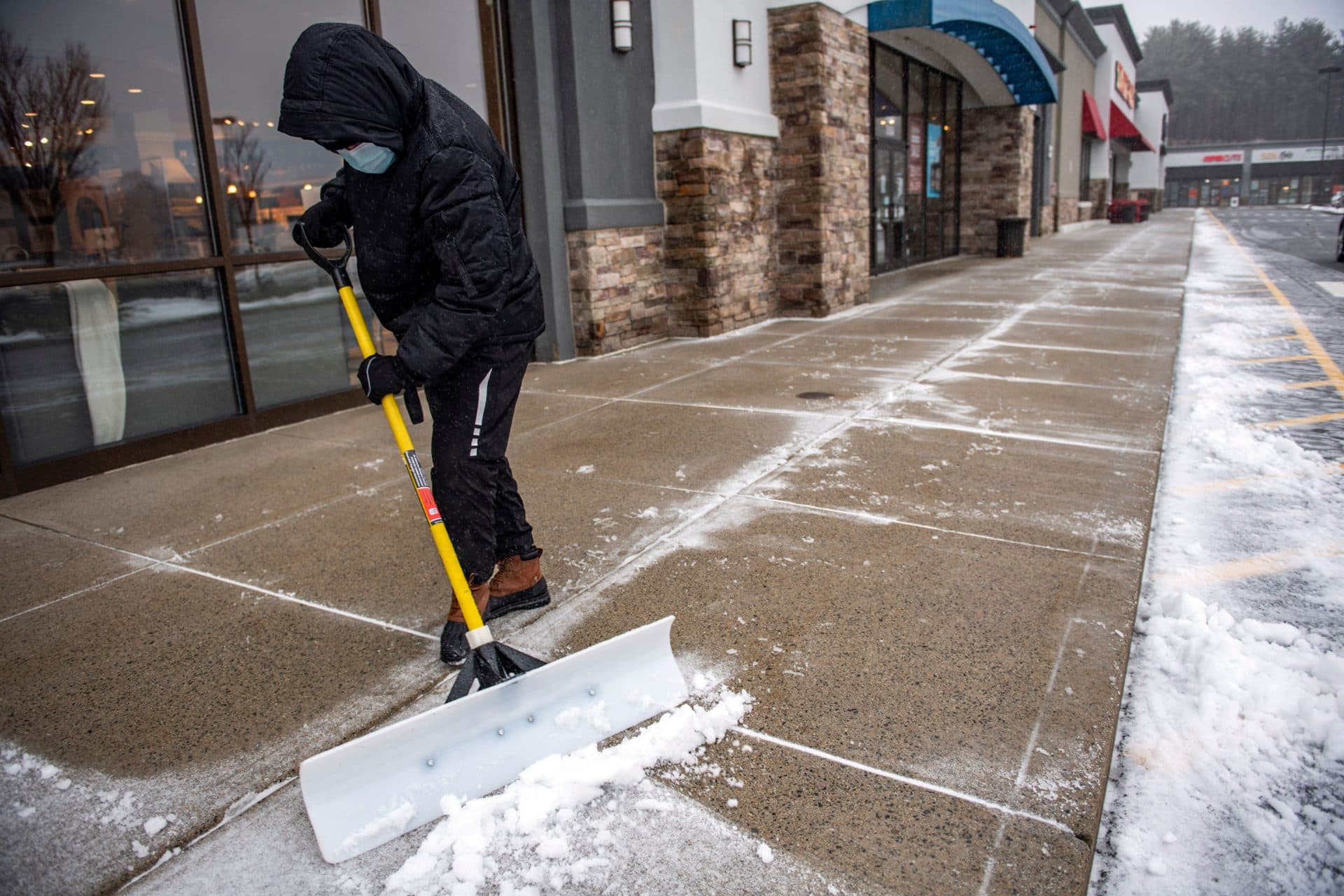 A worker clears snow and sleet from a shopping plaza sidewalk during a winter storm in Saugus. (Joseph Prezioso / AFP via Getty Images)