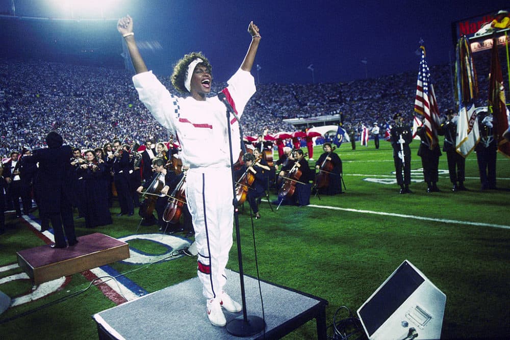Whitney Houston sings the National Anthem during the pregame show at Super Bowl XXV while tens of thousands of football fans wave tiny American flags in an incredible outburst of patriotism during the Persian Gulf War on Jan. 27, 1991. (Michael Zagaris/Getty Images)