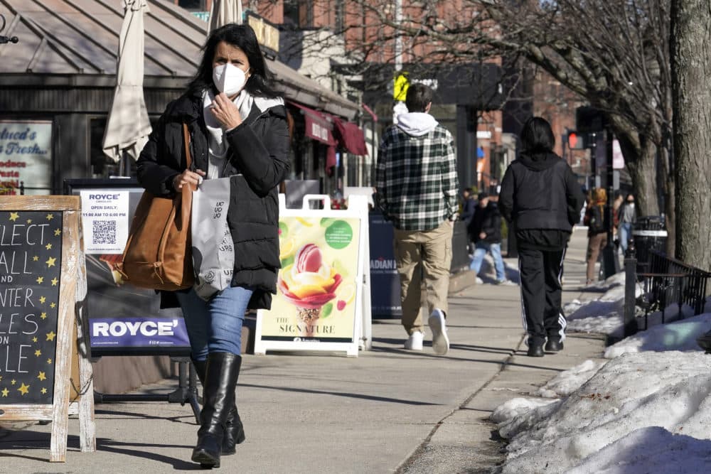 A pedestrian adjusts her mask, left, while walking on a sidewalk in the area of Newbury Street in Boston on Feb. 9. (Steven Senne/AP)