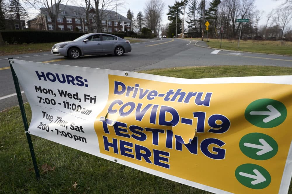 A motorist steers their car past a sign that calls attention to COVID-19 testing outside a testing location in Brockton. (Steven Senne/AP)