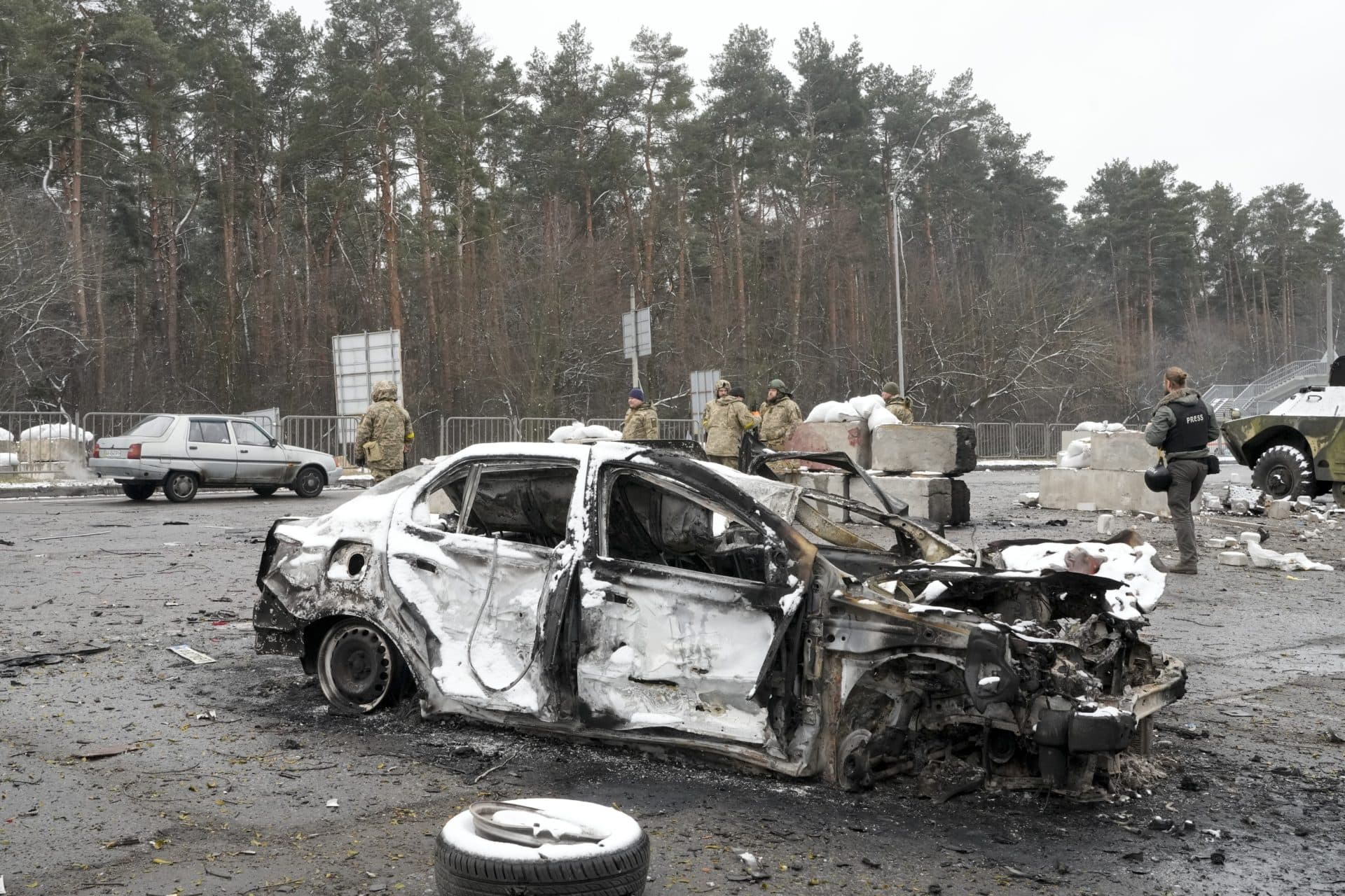 Ukrainian servicemen and volunteers of Ukraine's Territorial Defense Forces stand behind a damaged car at a checkpoint in Brovary, outside Kyiv, Ukraine on March 1. (Efrem Lukatsky/AP)