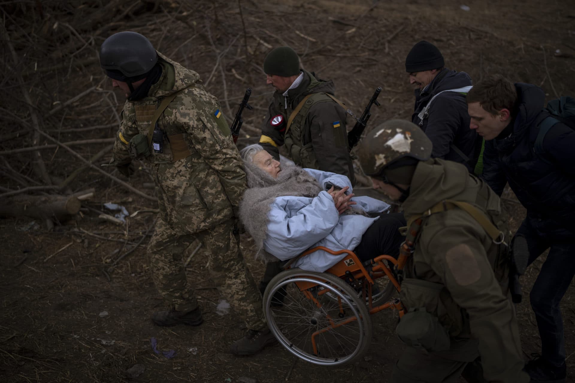 Ukrainian soldiers and militiamen carry a woman in a wheelchair as the artillery echoes nearby, while people flee Irpin on the outskirts of Kyiv, Ukraine, Monday, March 7, 2022. (Emilio Morenatti/AP)