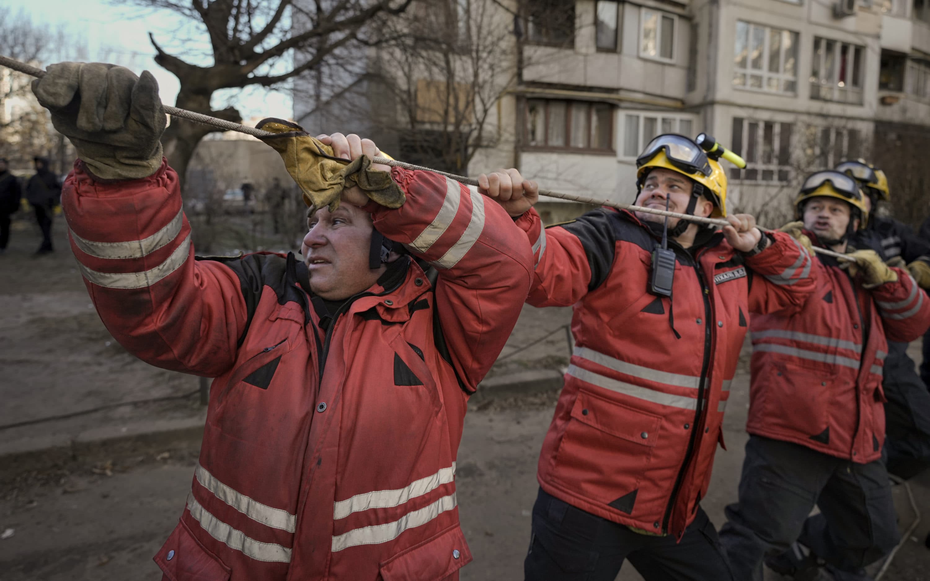 Firefighters pull a rope to direct the fall of a tree while working to extinguish a blaze in a destroyed apartment building after a bombing in a residential area in Kyiv, Ukraine, Tuesday, March 15, 2022. (Vadim Ghirda/AP)