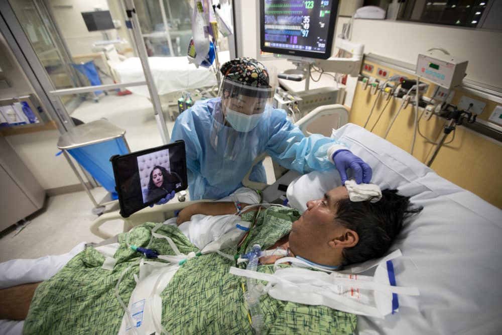 Registered Nurse Kat Yi holds an iPad up to Eduardo Rojas so that his wife Angelica Rojas inside the ICU at Providence St. Jude Medical Center Christmas Day on Friday, Dec. 25, 2020 in Fullerton, CA. (Francine Orr / Los Angeles Times via Getty Images)