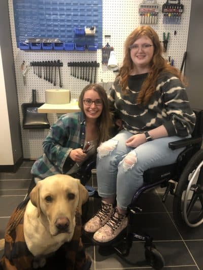 Aurorah Arndt (left) shows Sarah Ferguson a wheelchair maintenance hack, while her dog Hunter sits nearby (Photo courtesy Aurorah Arndt)