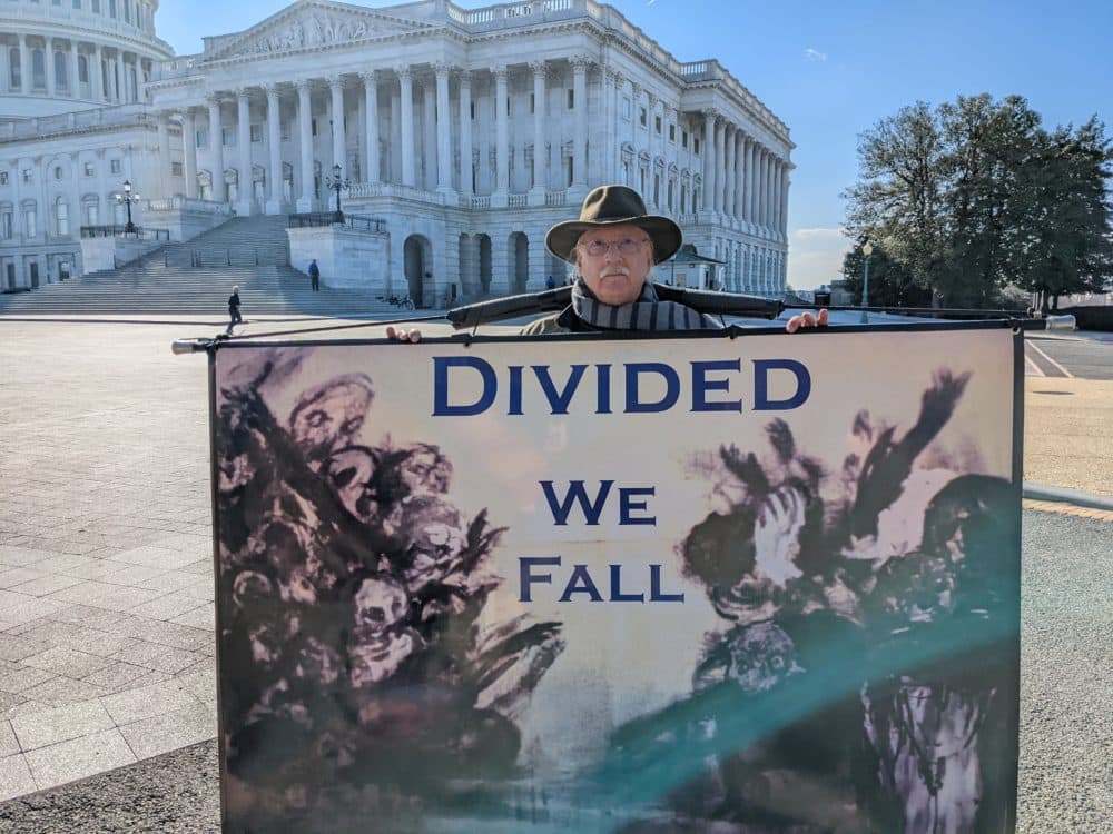 Stephen Parlato, an artist and activist, protests with signs outside of the Capitol building in Washington, D.C. (James Perkins Mastromarino/Here &amp; Now)