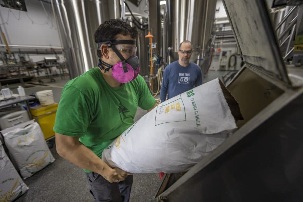 Matthew Steinberg watches as Joe Forte pours Wart Hog Wheat from Oechsner Farm in New York and malted by Valley Grain Milling in Hadley, Massachusetts into a mill at Exhibit 'A' Brewing to be used to brew one of their flagship beers, Cat’s Meow IPA. (Jesse Costa/WBUR)
