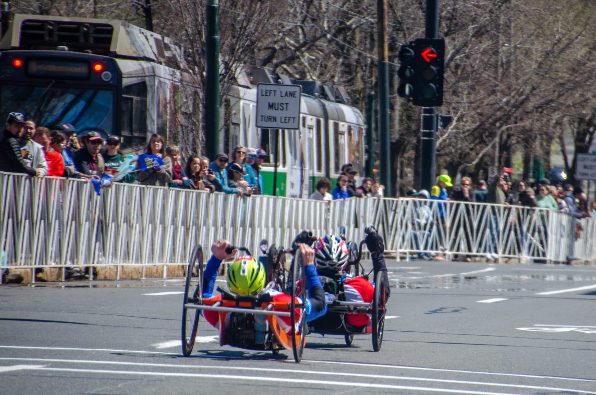 Handcycle race competitors at Mile 24 alongside the Green Line trolley in Brookline. (Sharon Brody/WBUR)