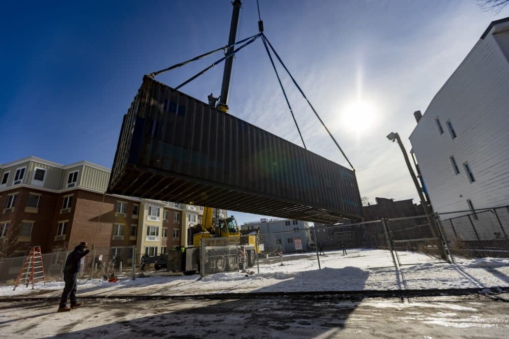 The shipping container holding the greenhouse is lifted onto the property at Eastie Farm. (Jesse Costa/WBUR)