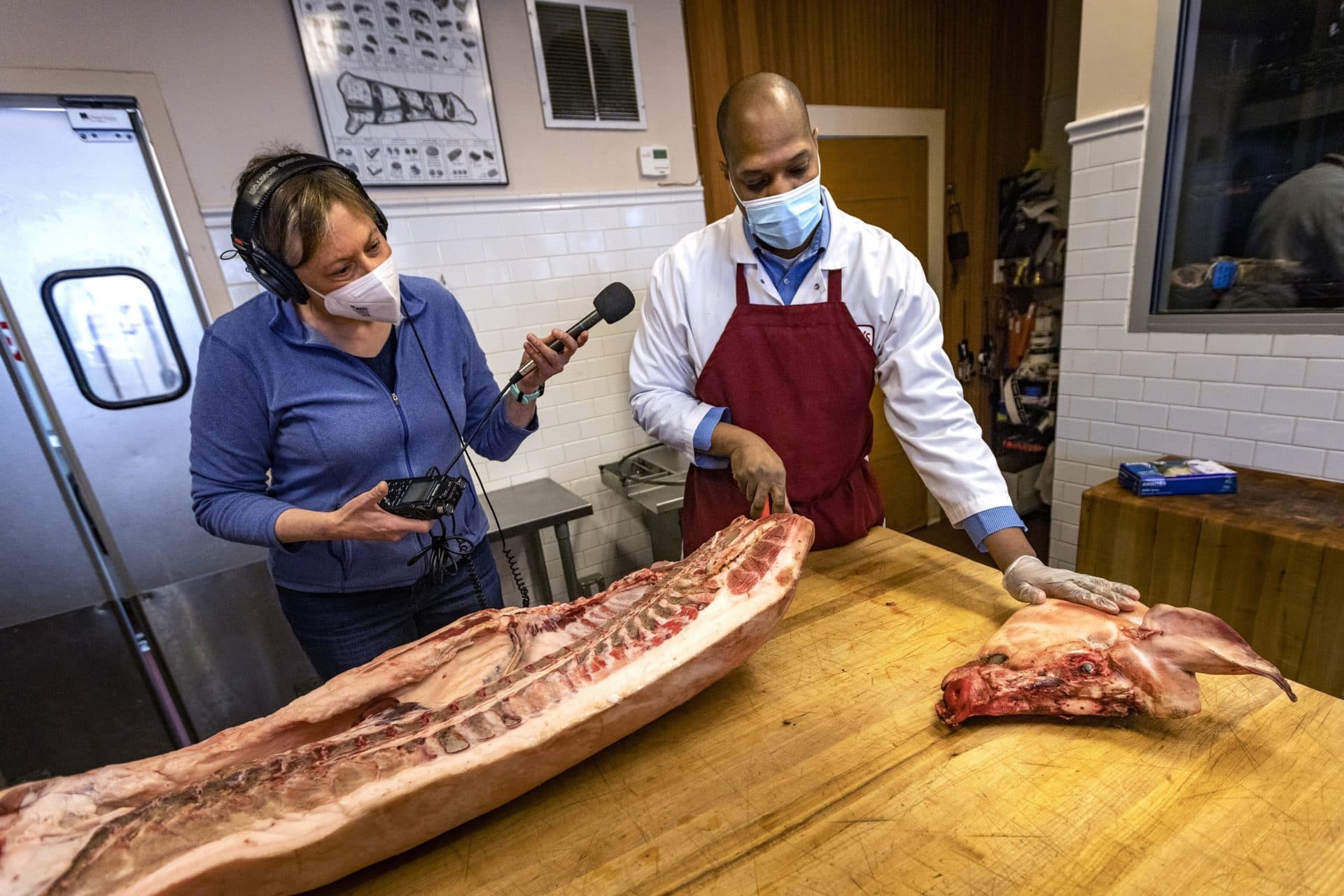 WBUR’s Barbara Moran listens as Christopher Walker, general manager of Savenor’s in Cambridge, explains not a single part of the pig will be wasted, including the head. (Jesse Costa/WBUR)
