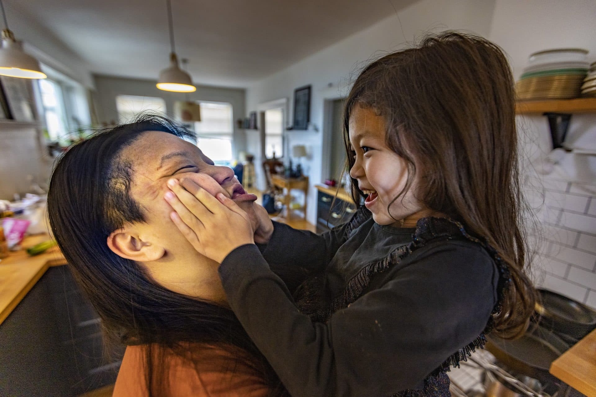 Mei Li’s daughter, Kira, smooshes Irene Li’s face as they play in the kitchen. (Jesse Costa/WBUR)