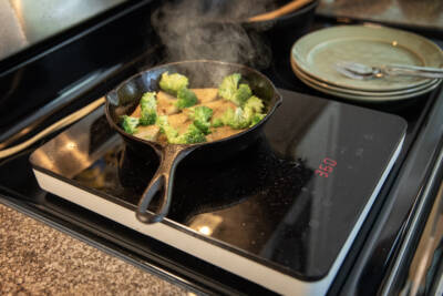 Tofu with garlic and broccoli sizzle on an induction portable cooktop. (Robin Lubbock/WBUR)