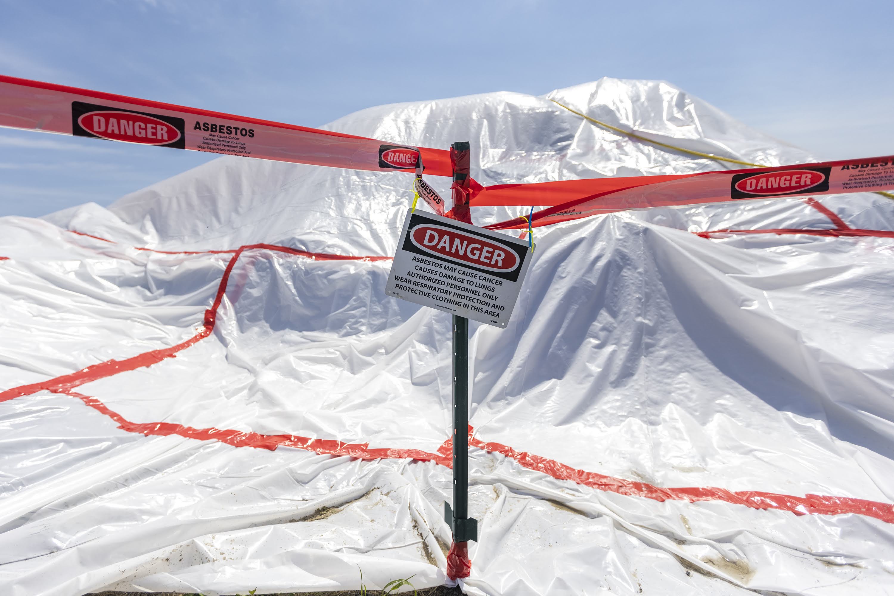 A covered pile of debris, with signs warning the presence of asbestos, at the Route 16 exit of Route 1 south, adjacent to the Prattville-Fitzpatrick Housing Development in Chelsea. (Jesse Costa/WBUR)
