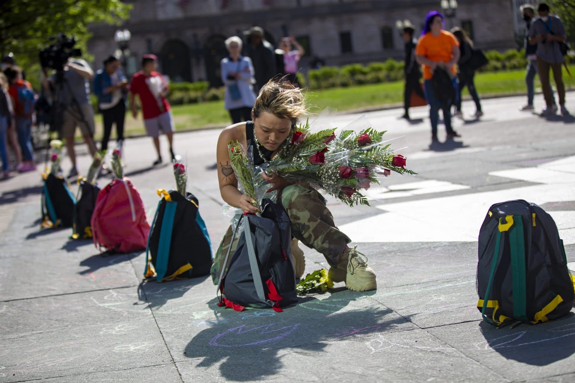 Ameya Okamoto places flowers into one of the 19 backpack which represent the students killed at Robb Elementary School in Uvalde, Texas. (Jesse Costa/WBUR)