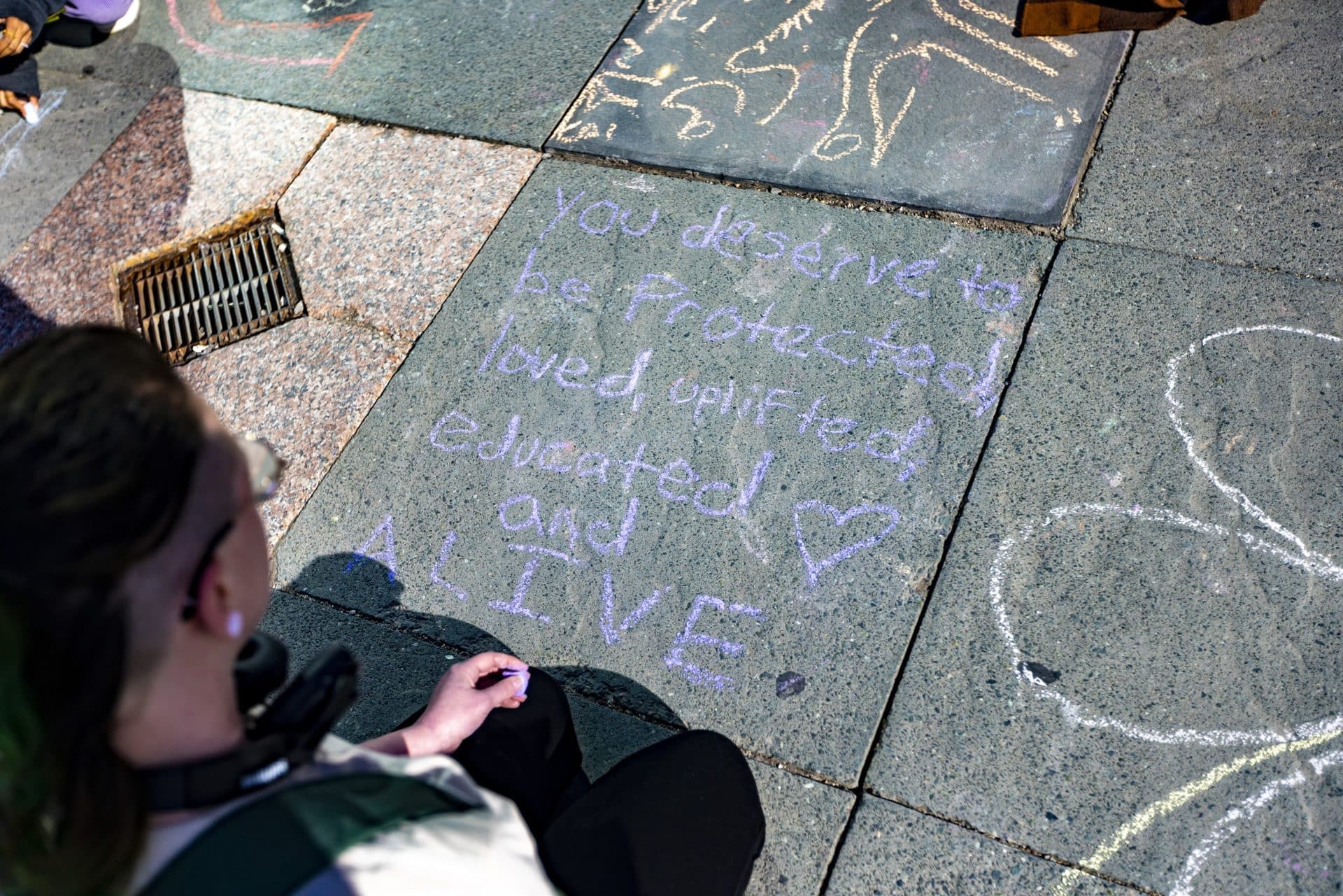 Charlie Jay writes a message in chalk on the plaza sidewalk in Copley Square at the memorial remembering the victims of the school shooting in Uvalde, Texas. (Jesse Costa/WBUR)