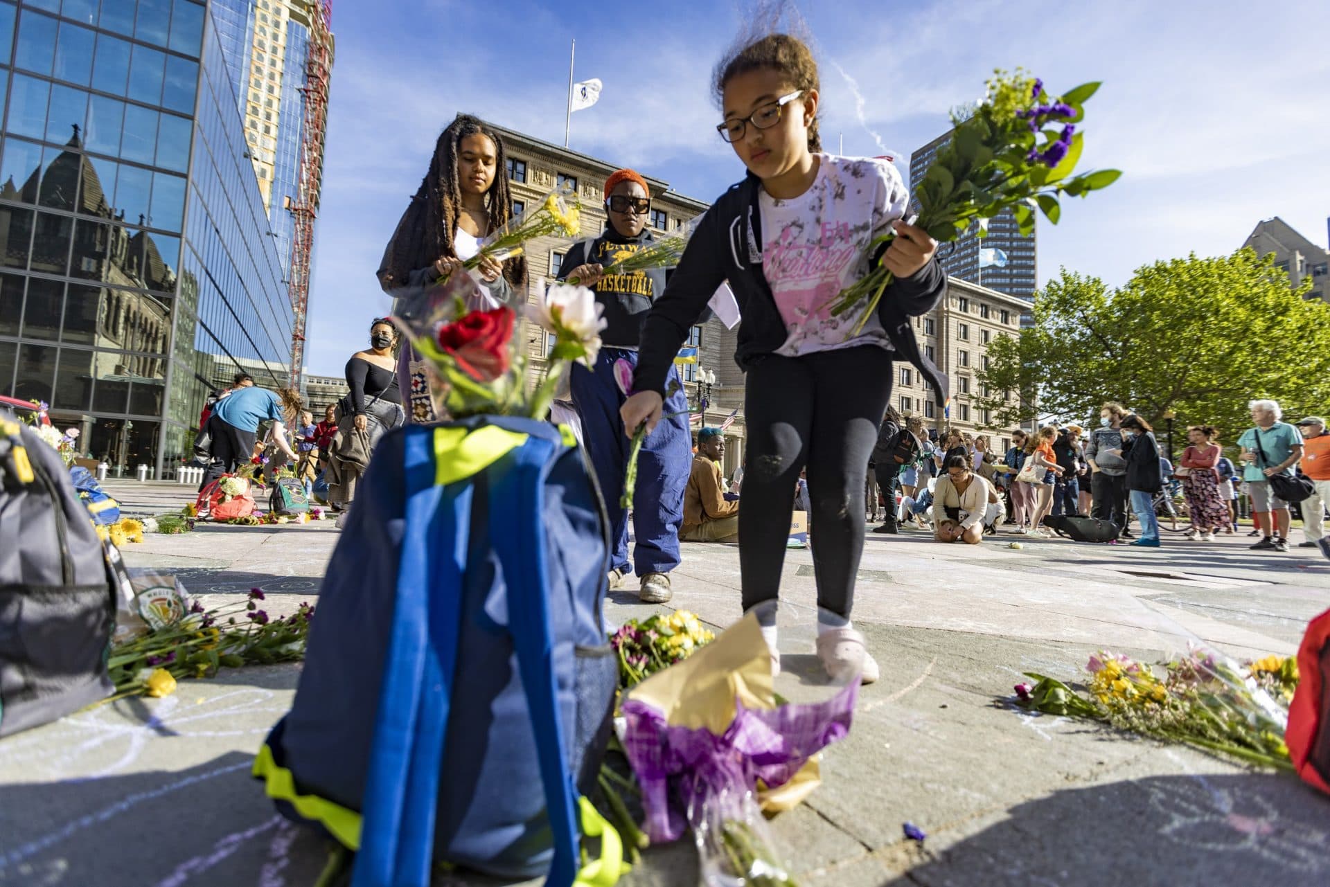 Ten-year-old Emma Lara leaves flowers at one of the backpacks at a memorial in Copley Square remembering the victims of the shooting at Robb Elementary School in Uvalde, Texas. (Jesse Costa/WBUR)