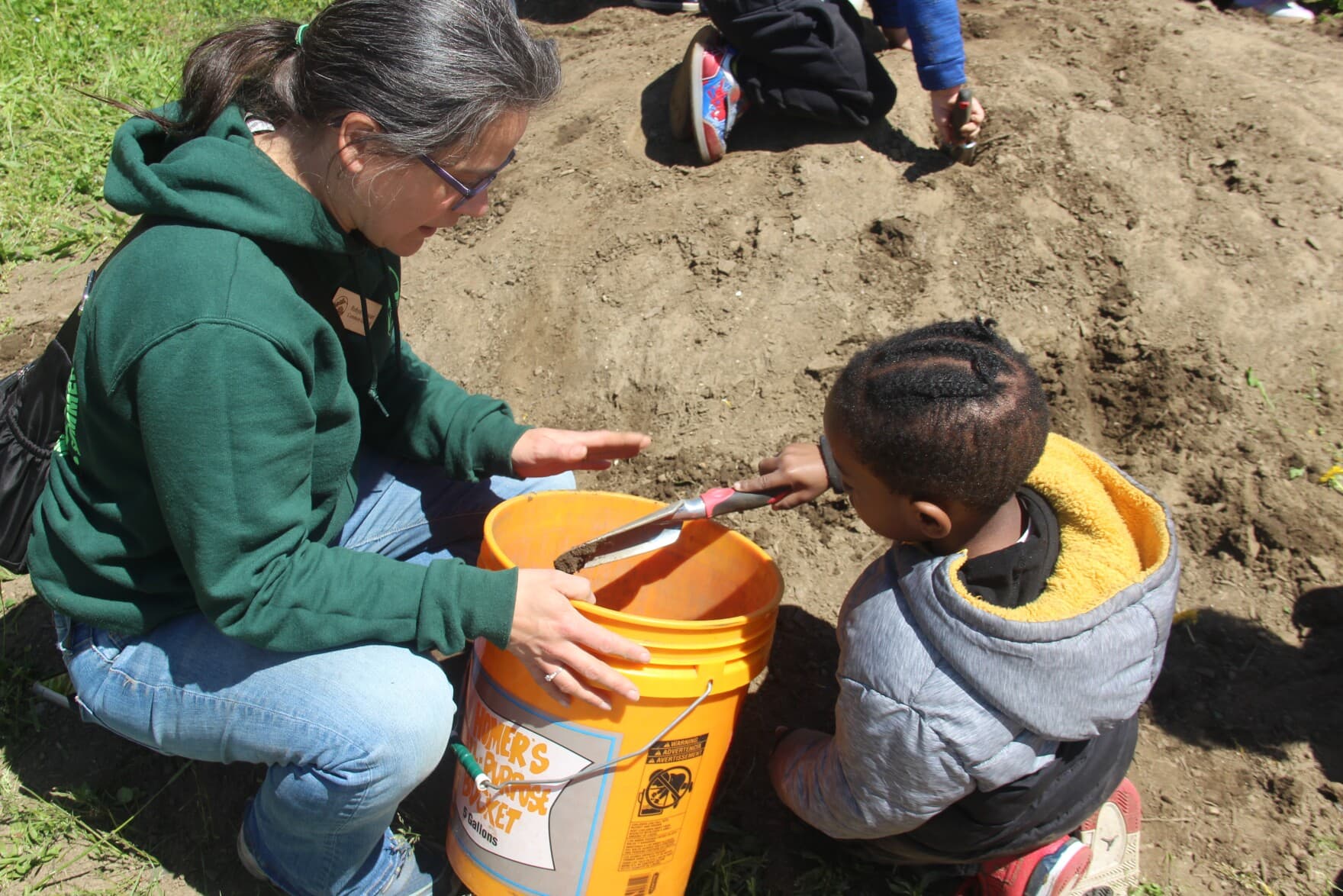 Common Ground’s Schoolyard Manager Robyn Stewart assists a young student in scooping soil at John S. Martinez magnet school in New Haven, Connecticut. (Megan Briggs/WSHU)