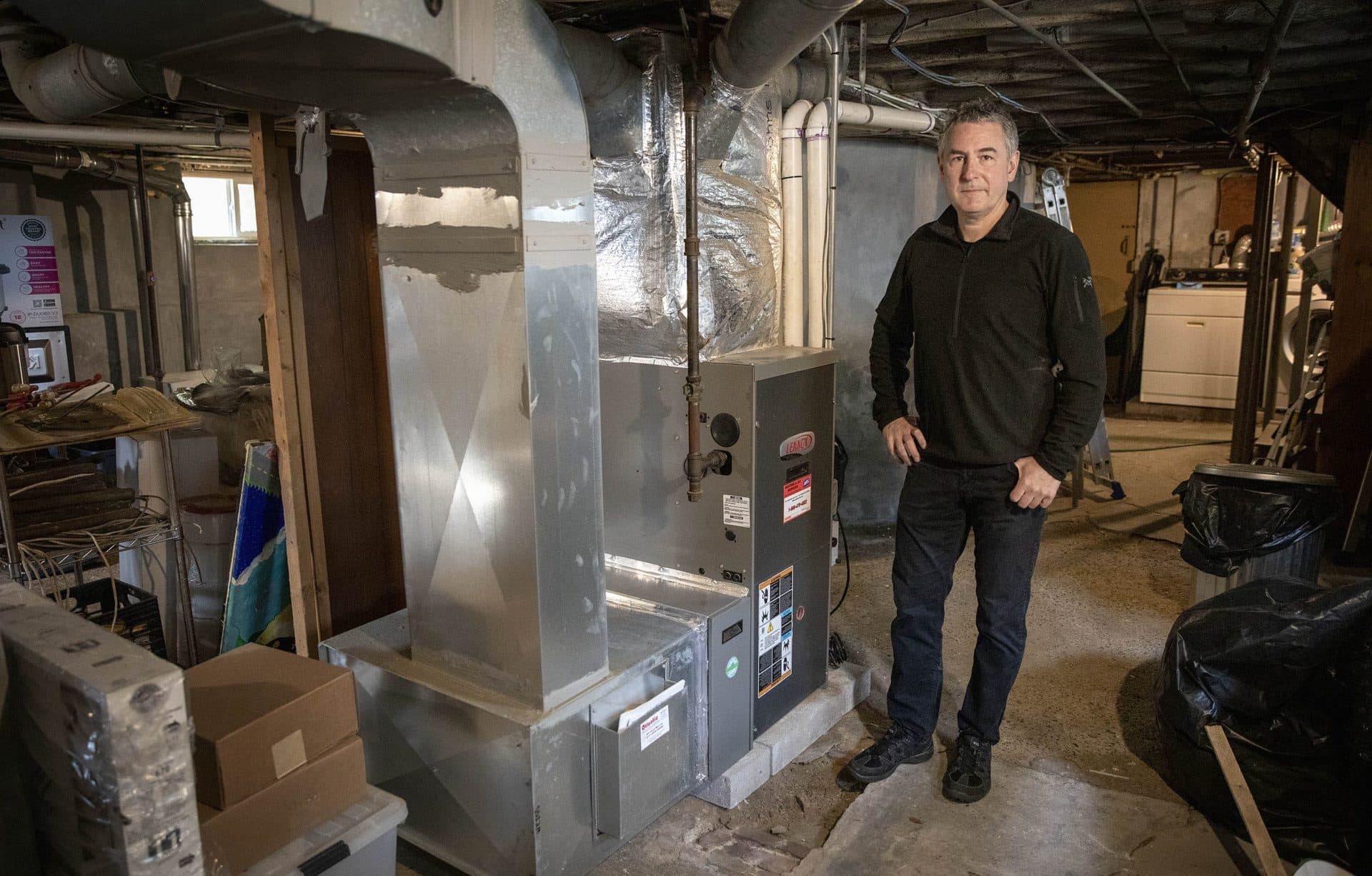 Jurgen Weiss in the basement of his home in Somerville with the gas furnace he currently uses to heat the building. (Robin Lubbock/WBUR)