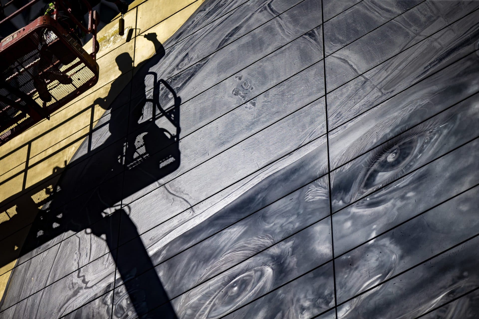 On a knuckle lift high in the air, Rob “ProblaK” Gibbs works on “Breathe Life Together,” the next mural to be featured on the façade of the Dewey Square Tunnel Air Intake Structure on the Rose Kennedy Greenway. (Jesse Costa/WBUR)