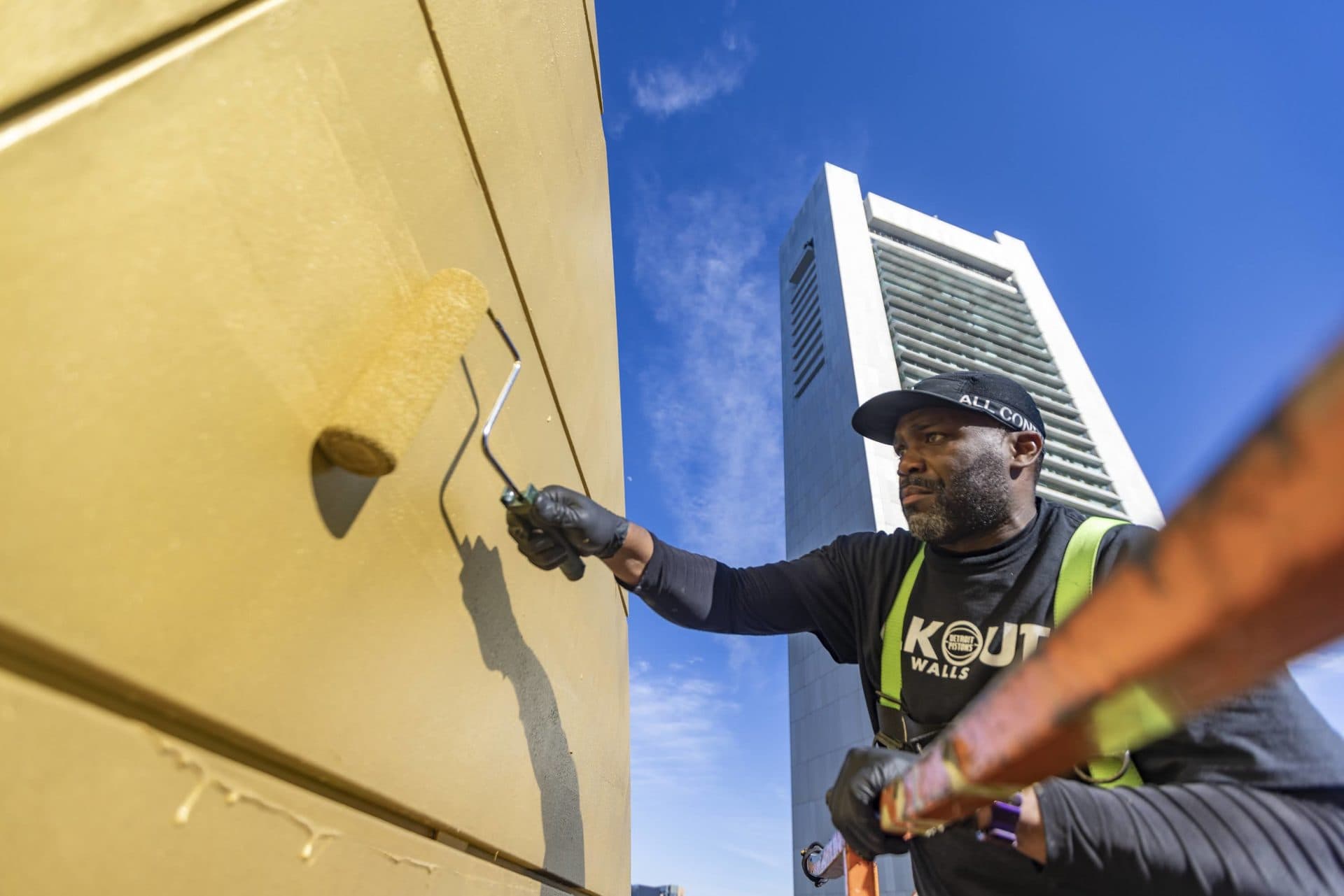 Rob “ProblaK” Gibbs applies gold paint with a roller as he creates “Breathe Life Together,” the next mural to be featured on the façade of the Dewey Square Tunnel Air Intake Structure on the Rose Kennedy Greenway. (Jesse Costa/WBUR)