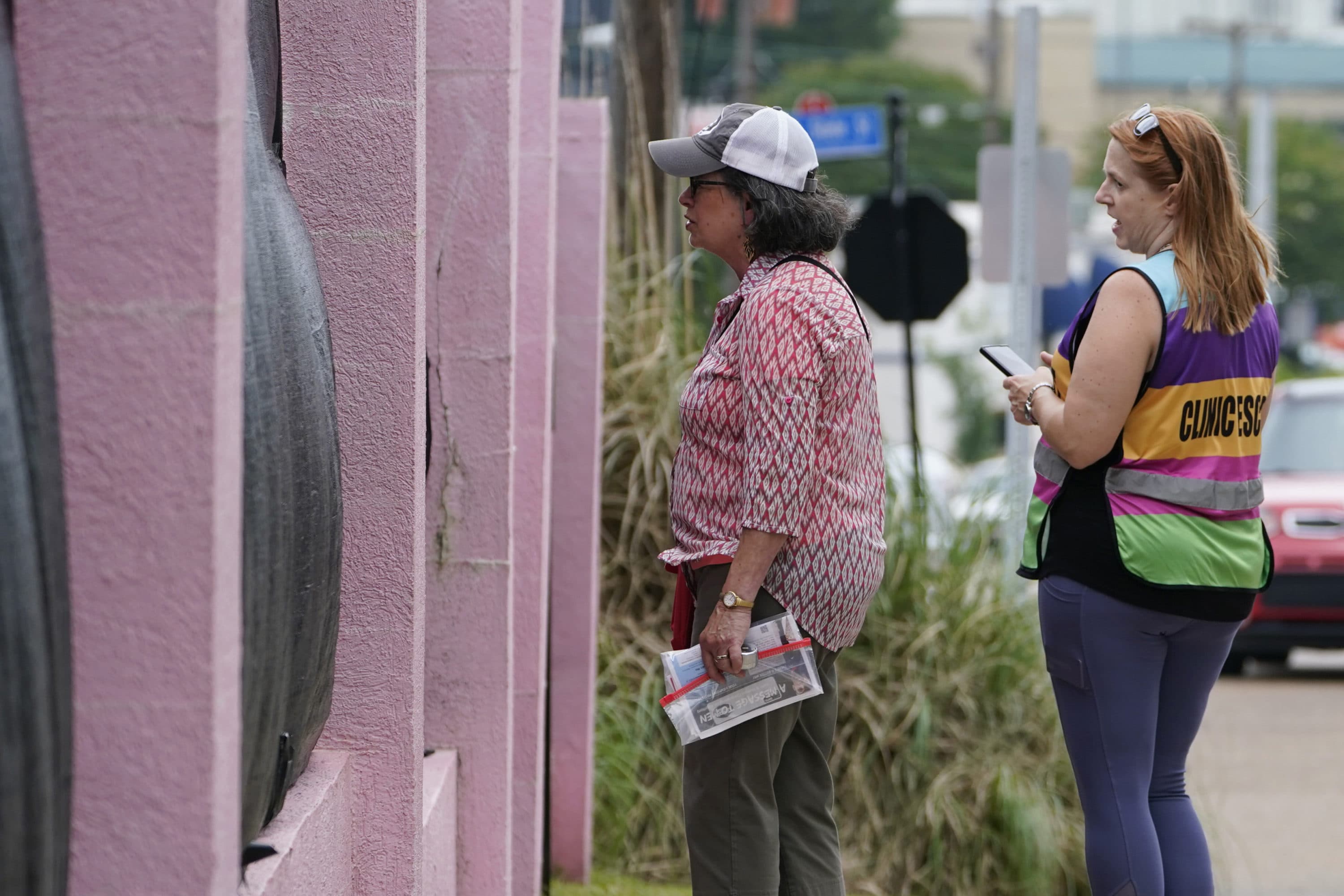 Pam Miller, an anti-abortion sidewalk counselor, left, speaks through the tarp draped fencing of the Jackson Womens Health Organization clinic, to an incoming patient at the front of the &quot;Pink House,&quot; while clinic escort Kim Gibson counters her statements, Thursday, May 20, 2021, in Jackson, Miss. (Rogelio V. Solis/AP)