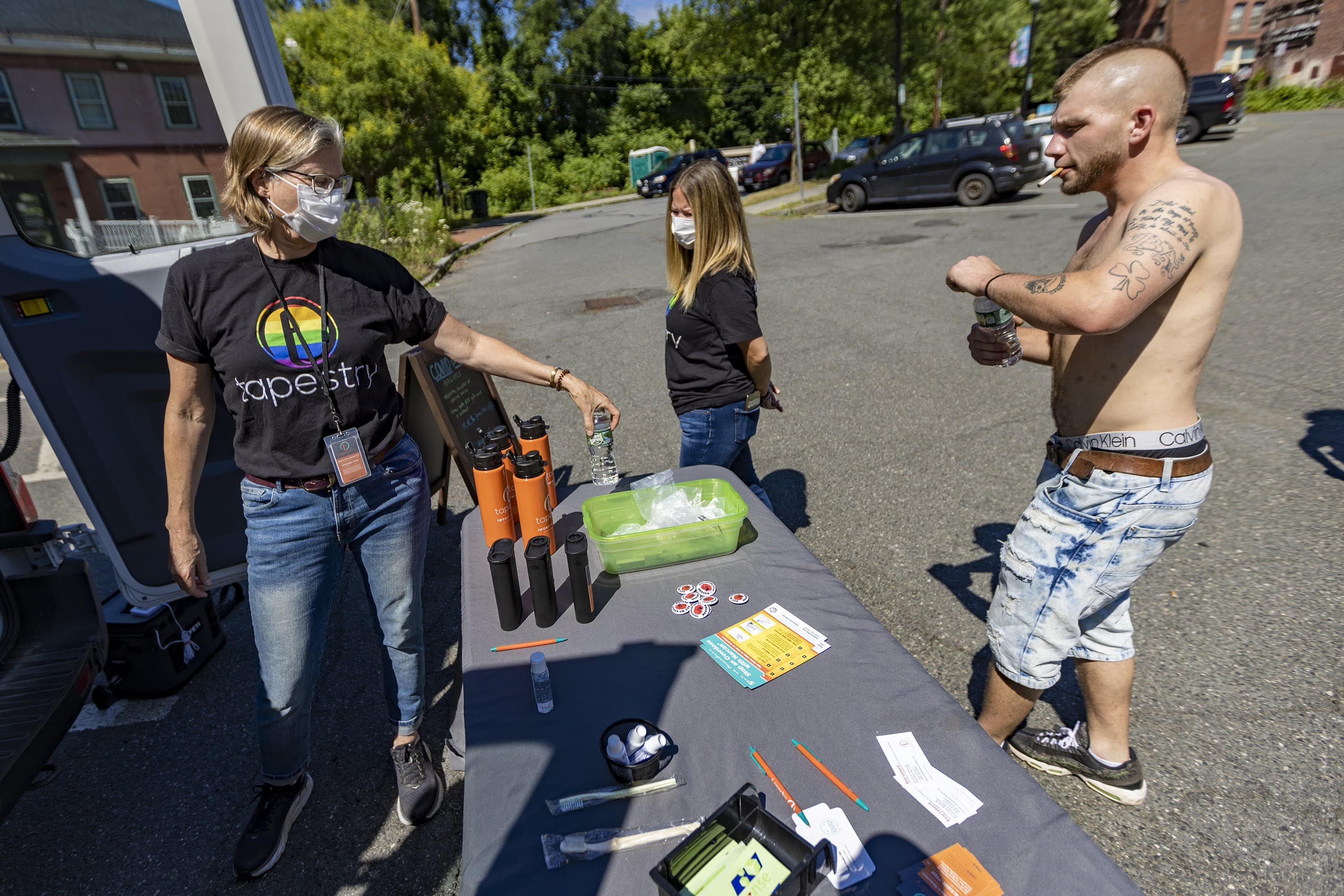 Tapestry Health nurse Katy Robbins hands bottles of water to Kyle as he visits the harm reduction mobile unit at Energy Park in Greenfield. (Jesse Costa/WBUR)