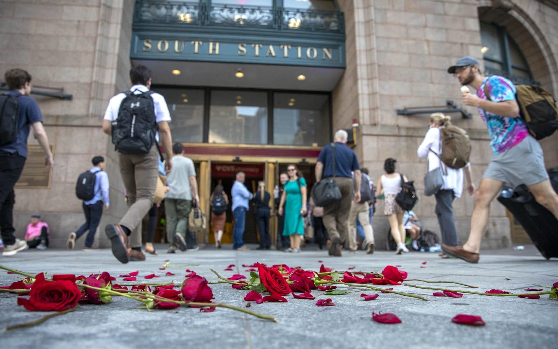 Commuters hurry past red roses scattered on the sidewalk at the entrance to South Station after a performance of artist Anne-Katrin Spiess' &quot;Death by Plastic.&quot; (Robin Lubbock/WBUR)