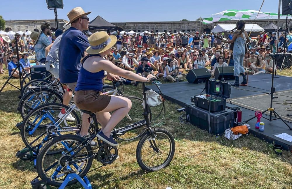 Madi Diaz, right, performs at the Newport Folk Festival's bike stage, powered in part by festivalgoers on stationary bicycles, left, Friday, July 22, 2022, in Newport, R.I. (Pat Eaton-Robb/AP)