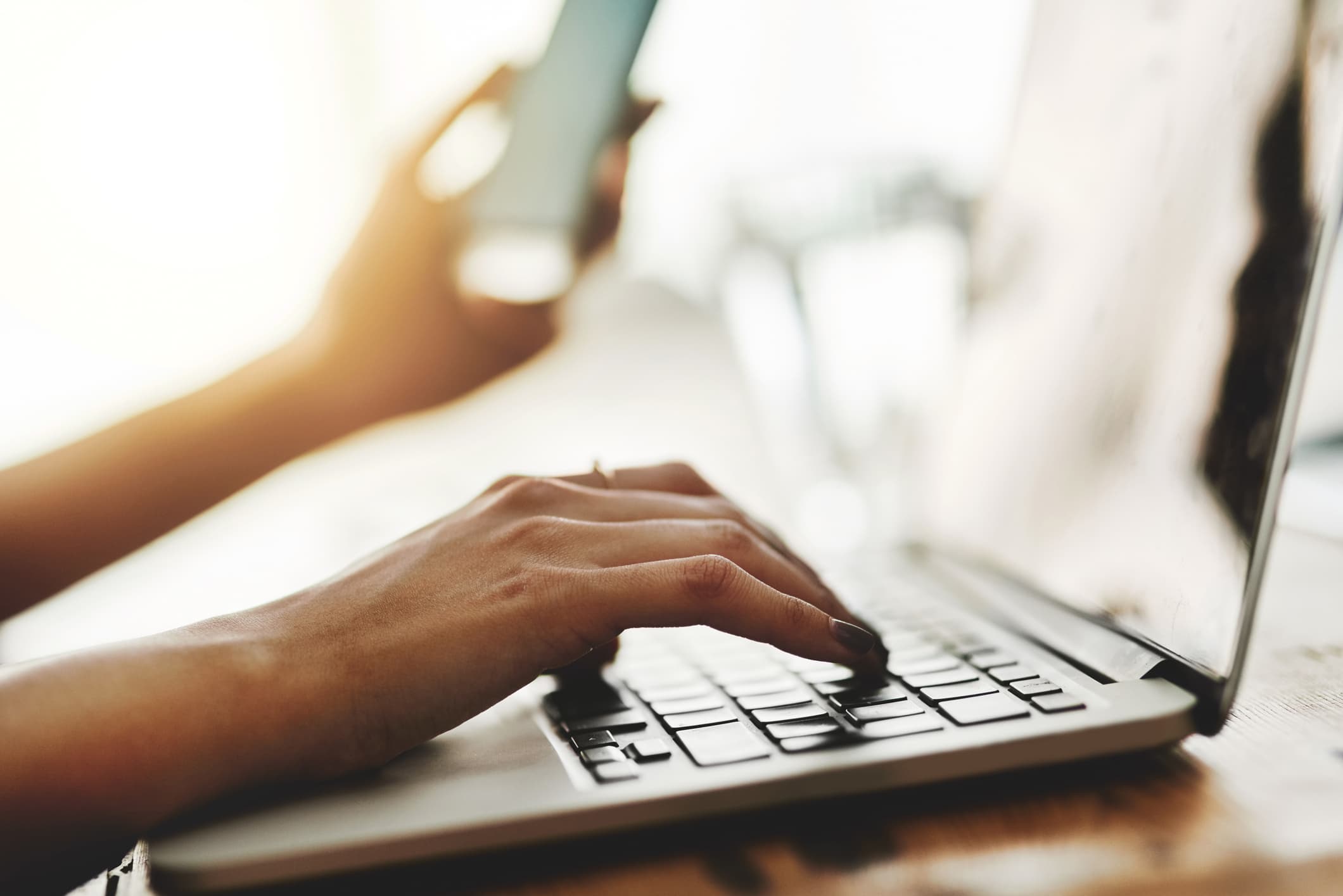 Closeup shot of an unidentifiable businesswoman using a cellphone and laptop while working in an office