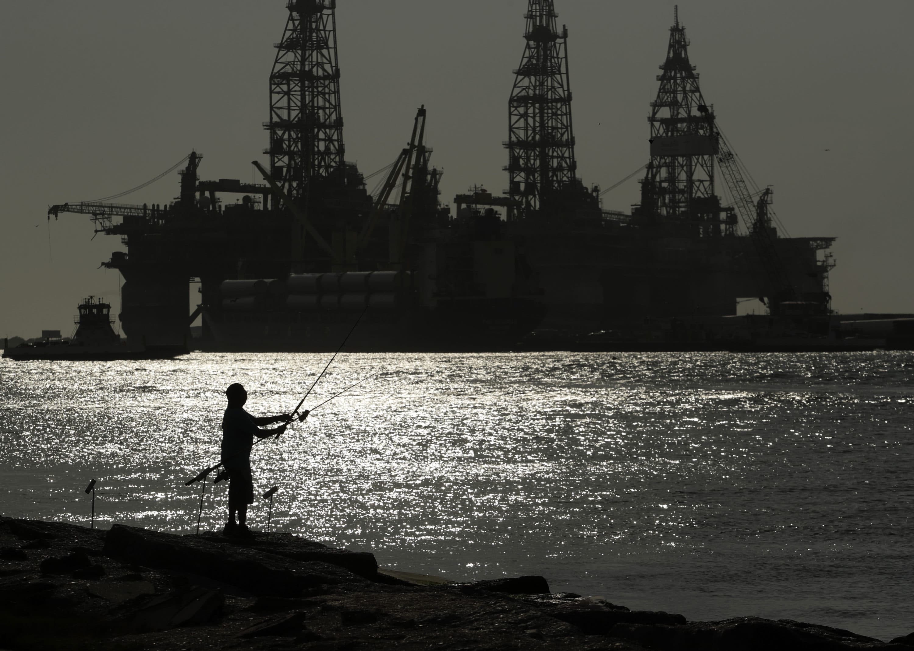 A man wears a face mark as he fishes near docked oil drilling platforms, on May 8, 2020, in Port Aransas, Texas. While the Inflation Reduction Act concentrates on clean energy incentives that could drastically reduce overall U.S. emissions, it also buoys oil and gas interests by mandating leasing of vast areas of public lands and off the nation’s coasts. (Eric Gay/AP)