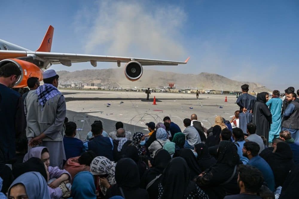 Afghan people sit as they wait to leave the Kabul airport in Kabul on August 16, 2021, after a stunningly swift end to Afghanistan's 20-year war, as thousands of people mobbed the city's airport trying to flee the group's feared hardline brand of Islamist rule. (Wakil Kohsar /Getty Images)