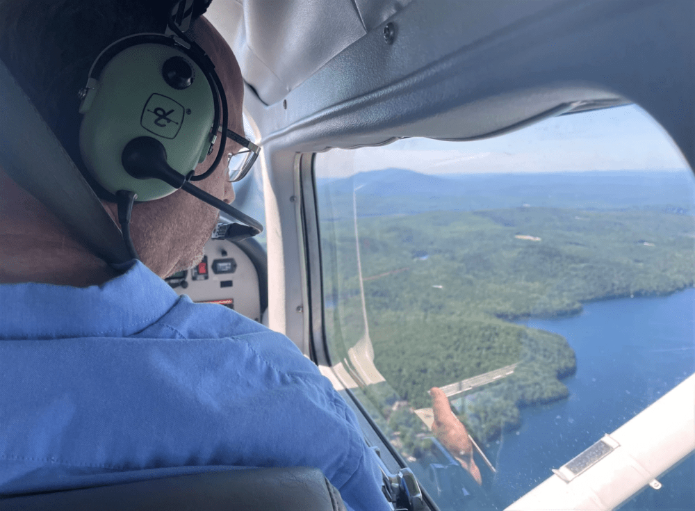 Forester Kyle Lombard looks out the window of the small airplane, searching for damage in the New Hampshire forest below. (Mara Hoplamazian/NHPR)
