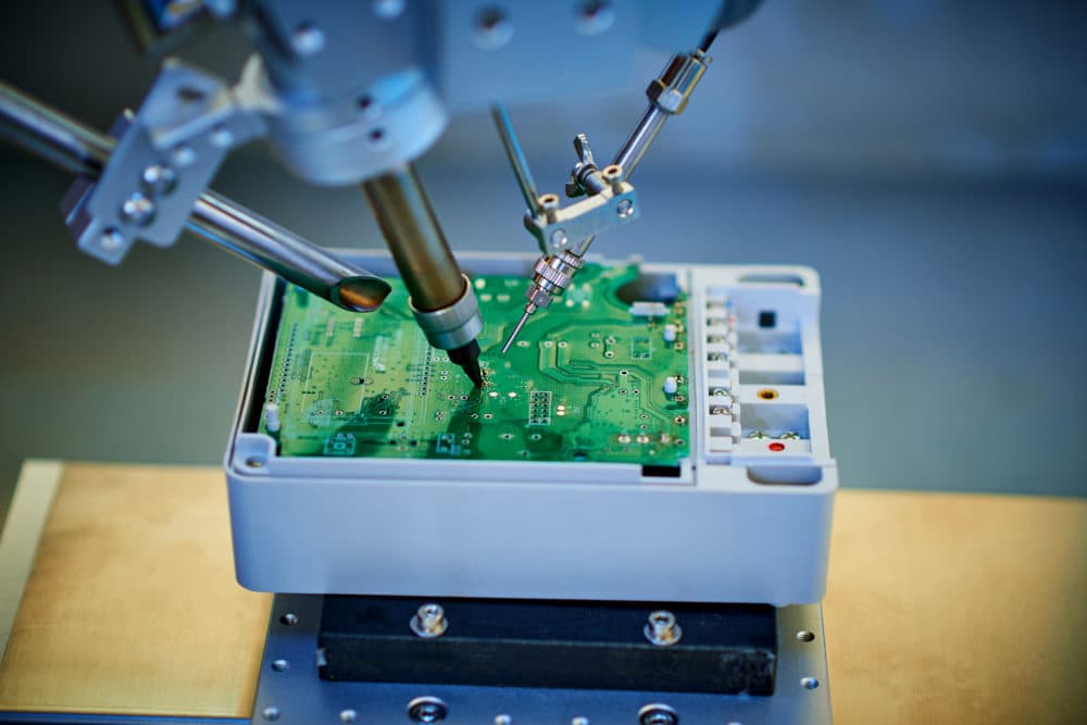 Robotic arm welding and installing component at semiconductor circuit board on workbench. (Getty Images)