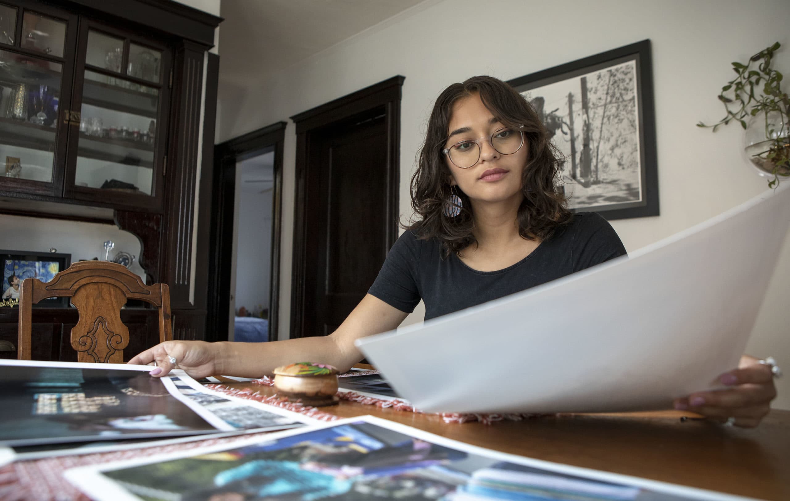 Documentary photographer Iaritza Menjivar looks through prints of her work. (Robin Lubbock/WBUR)