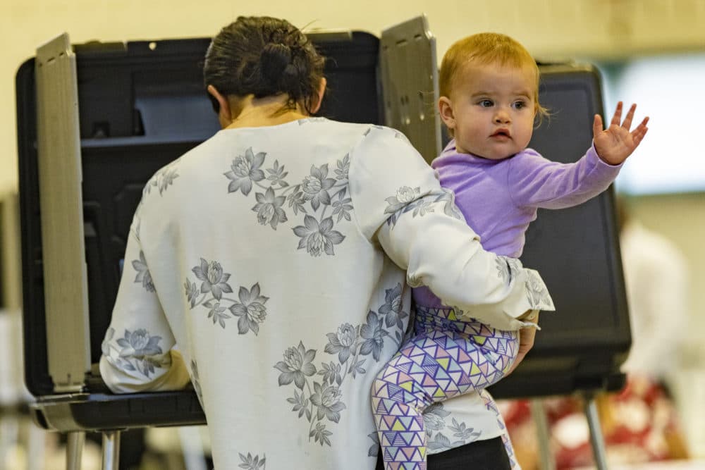 A baby waves to poll volunteers as her mother votes at the Williams Junior High School Auditorium in Chelsea on Primary Election Day. (Jesse Costa/WBUR)