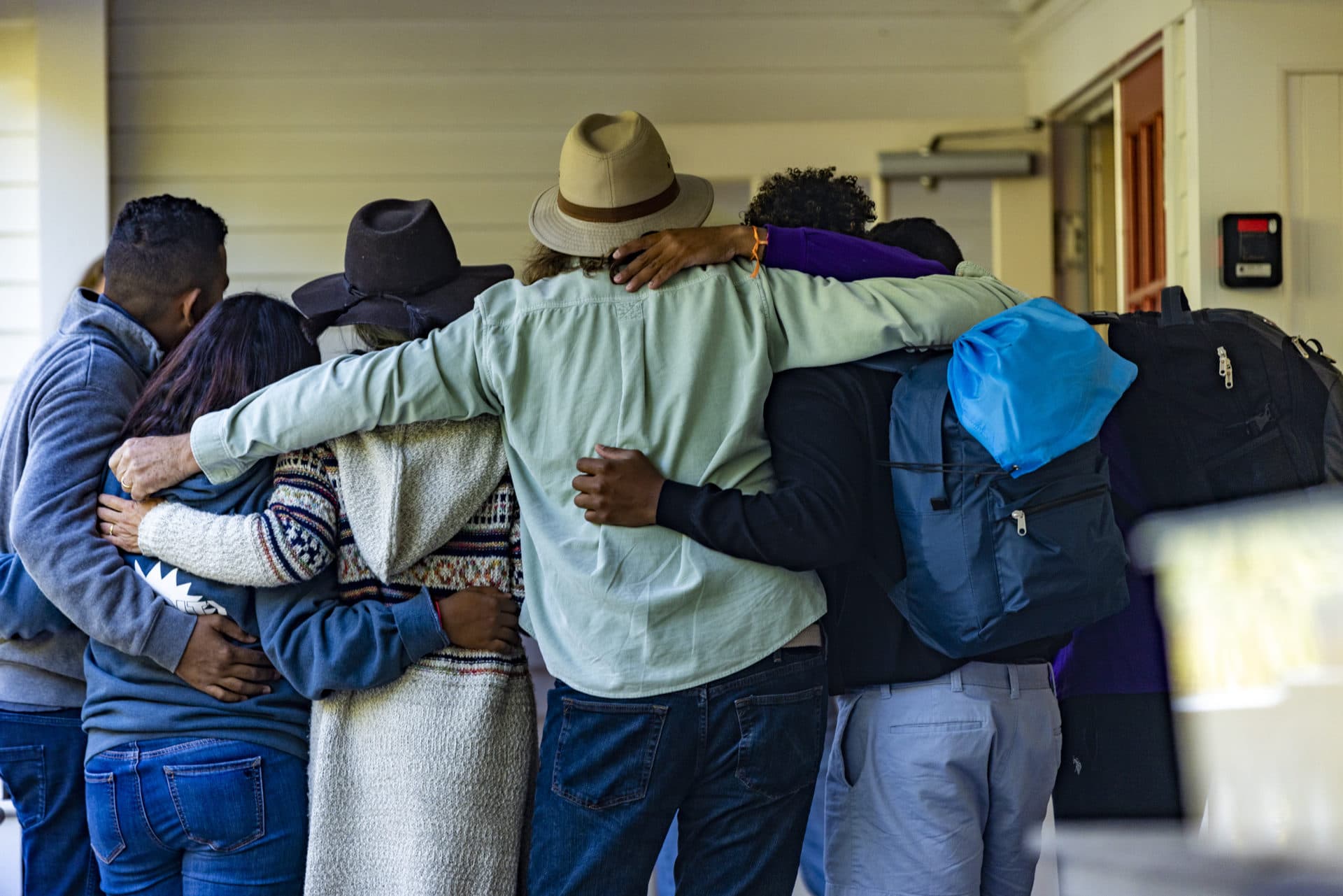 Immigrants and volunteers stand arm-in-arm in a huddle as the migrants depart St. Andrews Parish House in Edgartown. (Jesse Costa/WBUR)
