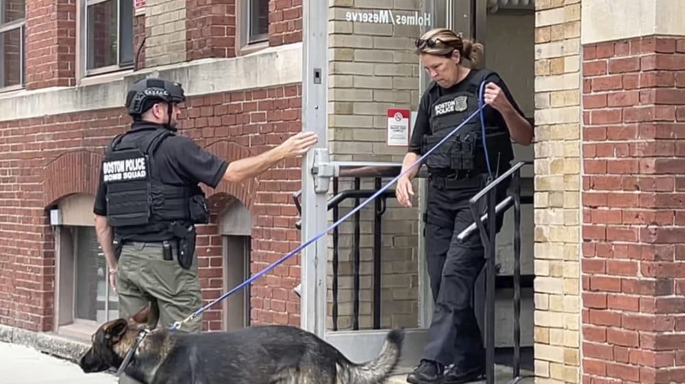 In a still photograph taken from video, a Boston Police bomb squad officer, left, and a K-9 unit officer, right, depart a building on the campus of Northeastern University, Sept. 14, 2022, in Boston. (Rodrique Ngowi/AP)