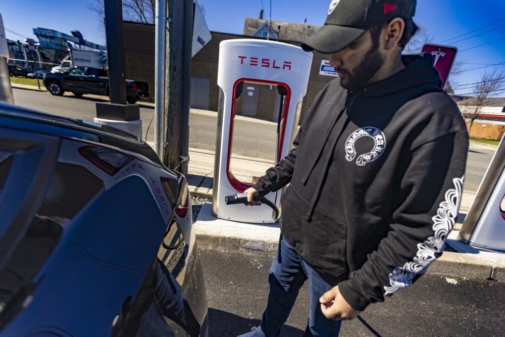 Roger Souza plugs in his Model Y Performance Tesla at a charging station on McGrath Highway in Somerville. (Jesse Costa/WBUR)