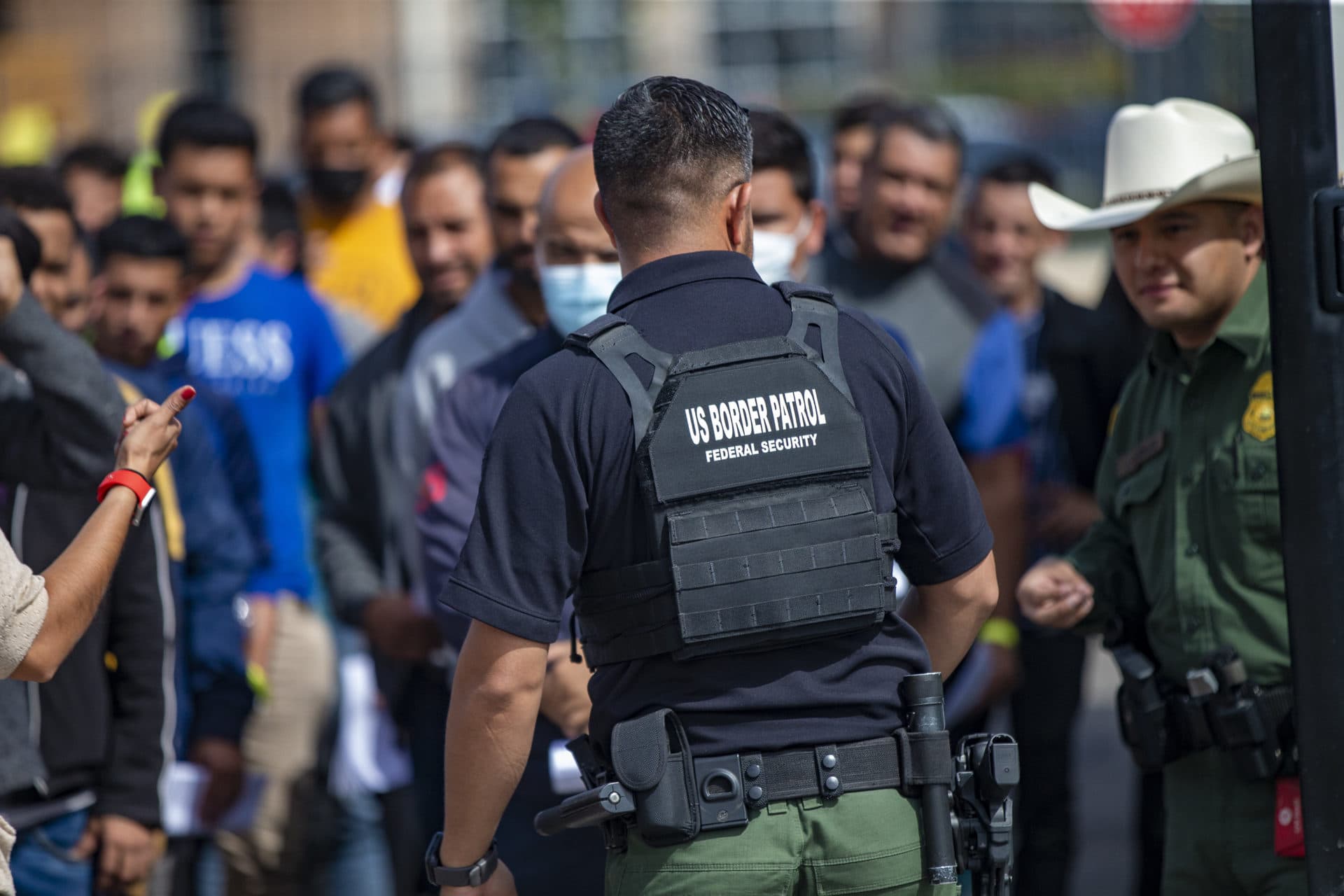 A U.S. Border Patrol agent watches as immigrants line up to be processed after being picked up at the U.S-Mexico border at the Immigration Welcome Center in El Paso. (Jesse Costa/WBUR)