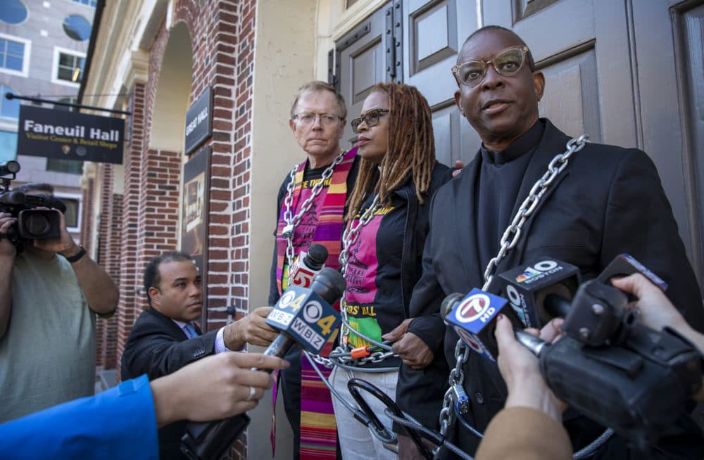 Rev. Dr. Kevin Peterson (far right) addresses reporters at the entrance of Faneuil Hall, demanding the name of the hall should be changed. (Robin Lubbock/WBUR)