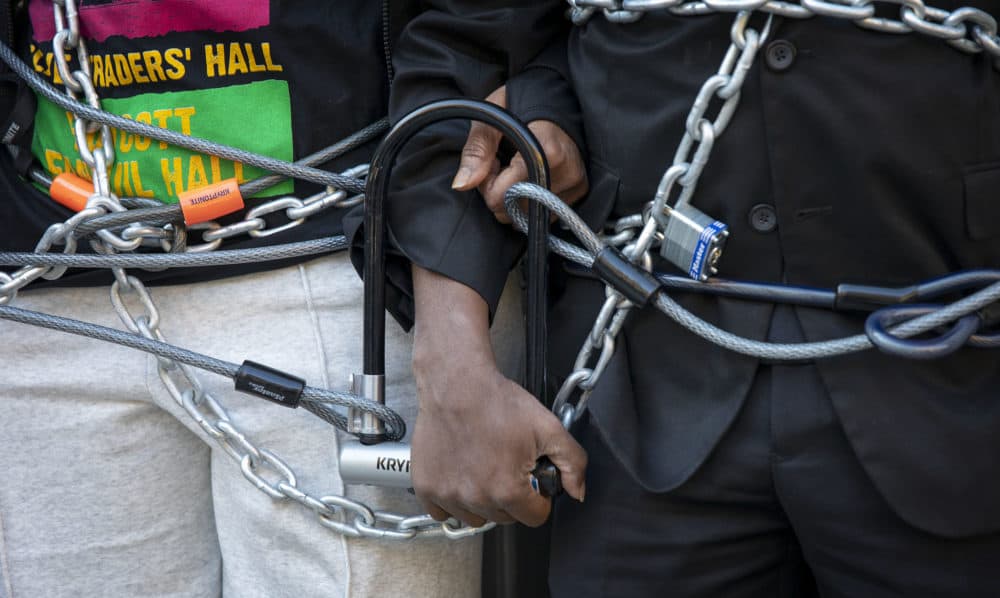 Pastor Valerie Copeland's and Rev. Dr. Kevin Peterson's arms locked together and wrapped in chains at their protest at the entrance of Faneuil Hall, demanding the name of the hall should be changed. (Robin Lubbock/WBUR)