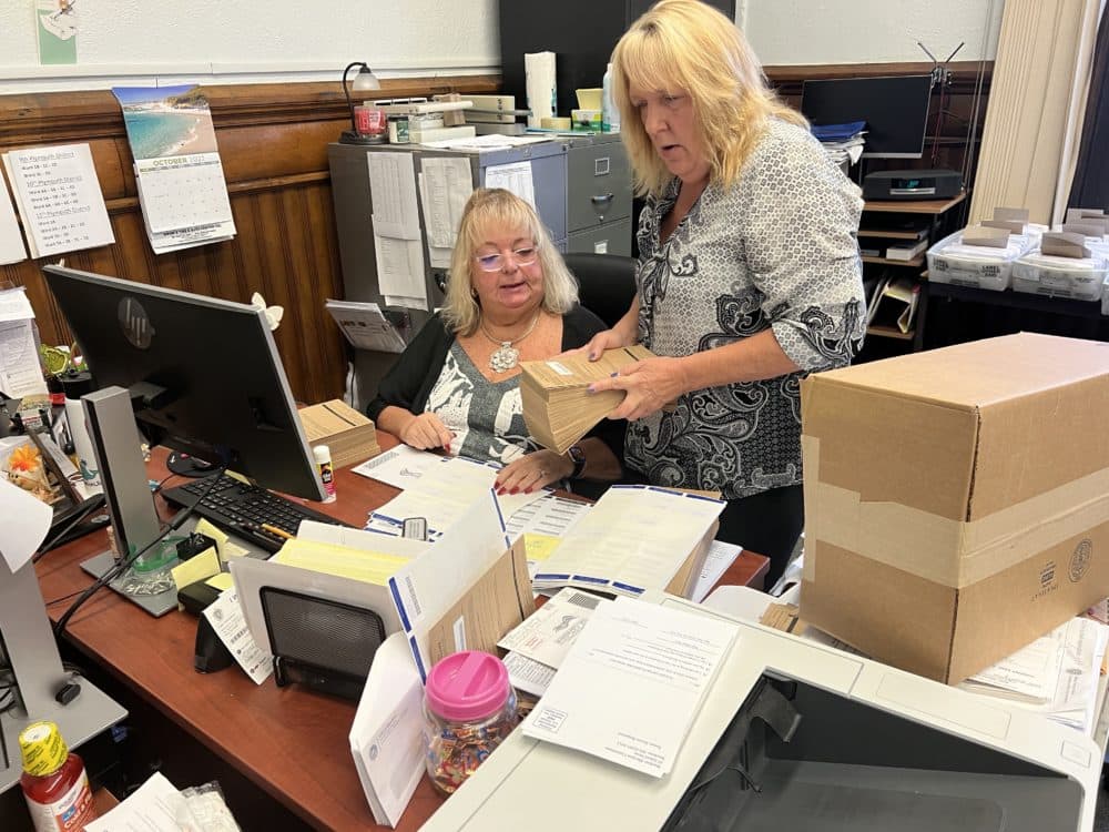 Brockton Election Executive Director Cynthia Scrivani confers with election department staffer Laurie Lemieux as they put ballots into envelopes to be sent to voters. (Steve Brown/WBUR)