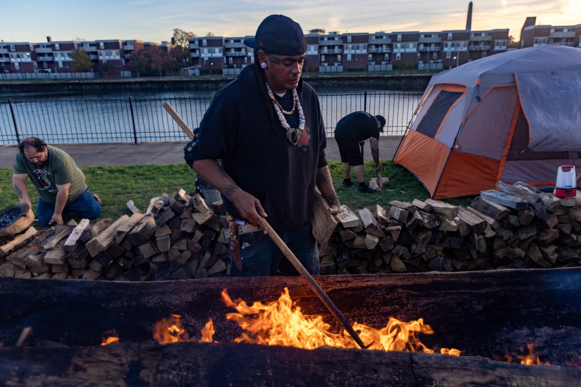 Andre StrongBearHeart, cultural steward of the Nipmuc tribe, tends to the fire while burning a traditional mishoon, or canoe, at the Charlestown Little Mystic Boat Slip. It is the first time in many years a mishoon has been made in the city of Boston. (Jesse Costa/WBUR)