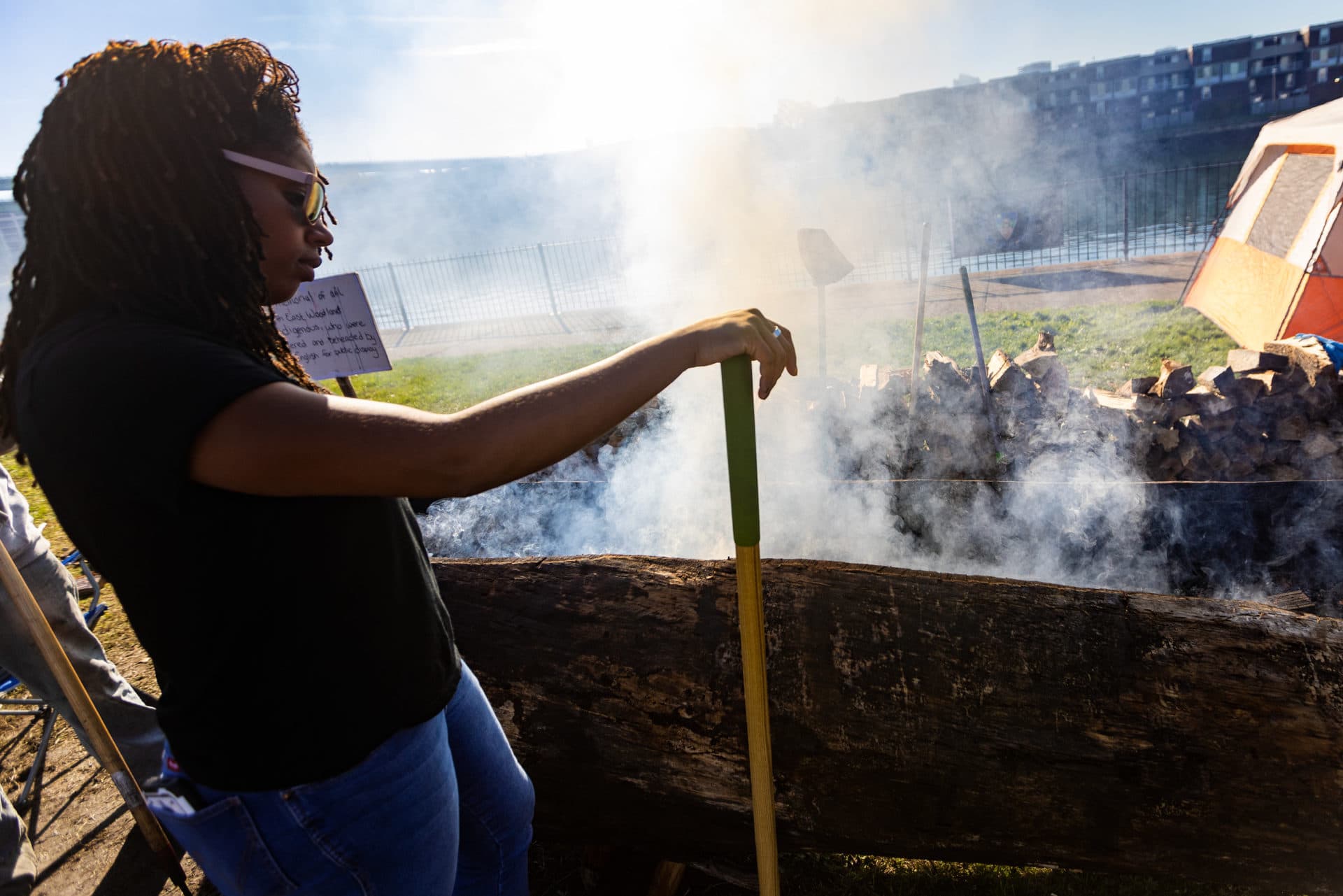 Jenny Oliver, a member of the Massachusett Tribe at Ponkapoag, watches the fire while burning a traditional mishoon at the Charlestown Little Mystic Boat Slip. (Jesse Costa/WBUR)
