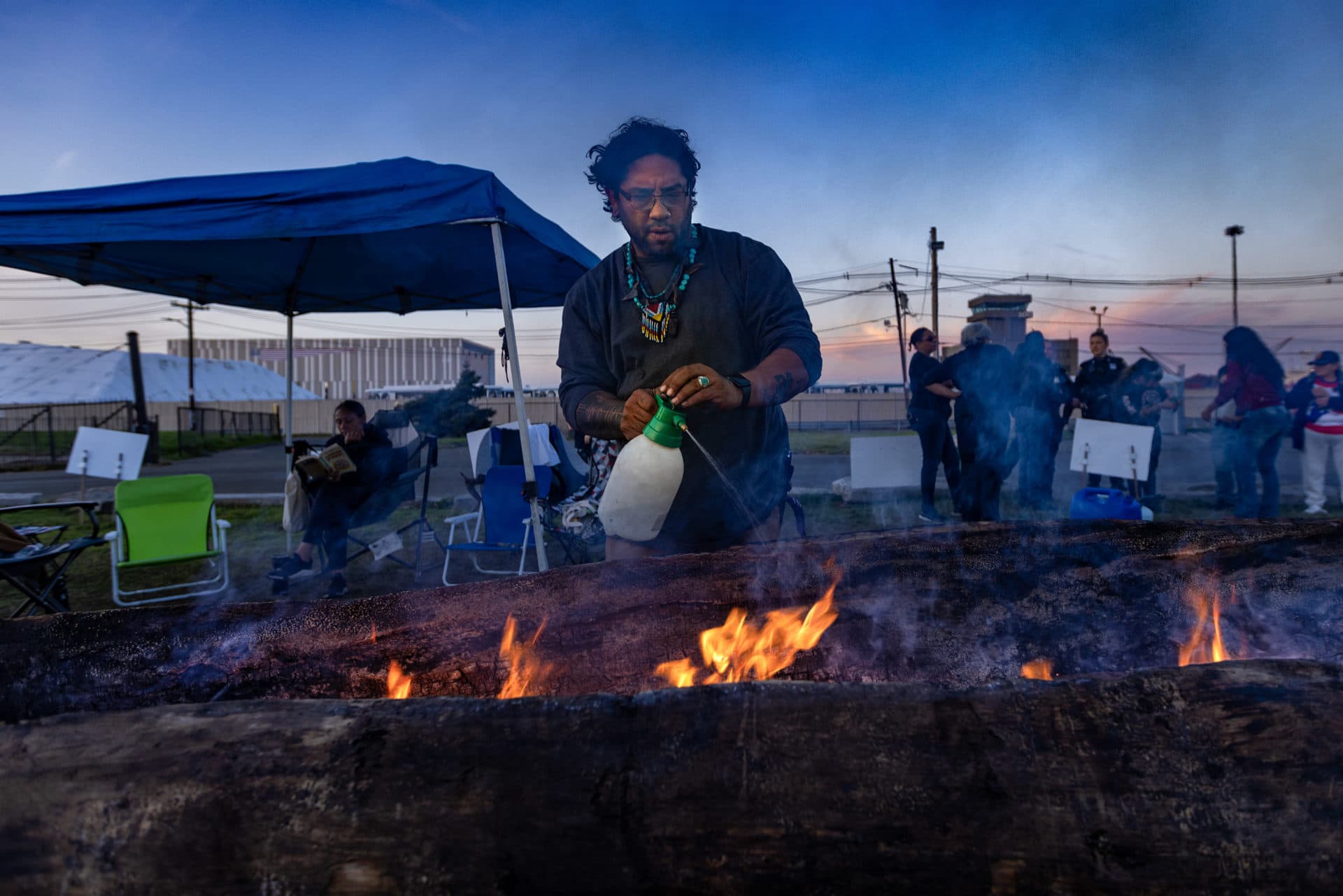 Dylan Lach, of the Chappaquiddick Wompanoag tribe, sprays water onto the sides of the mishoon to keep them from burning. (Jesse Costa/WBUR)