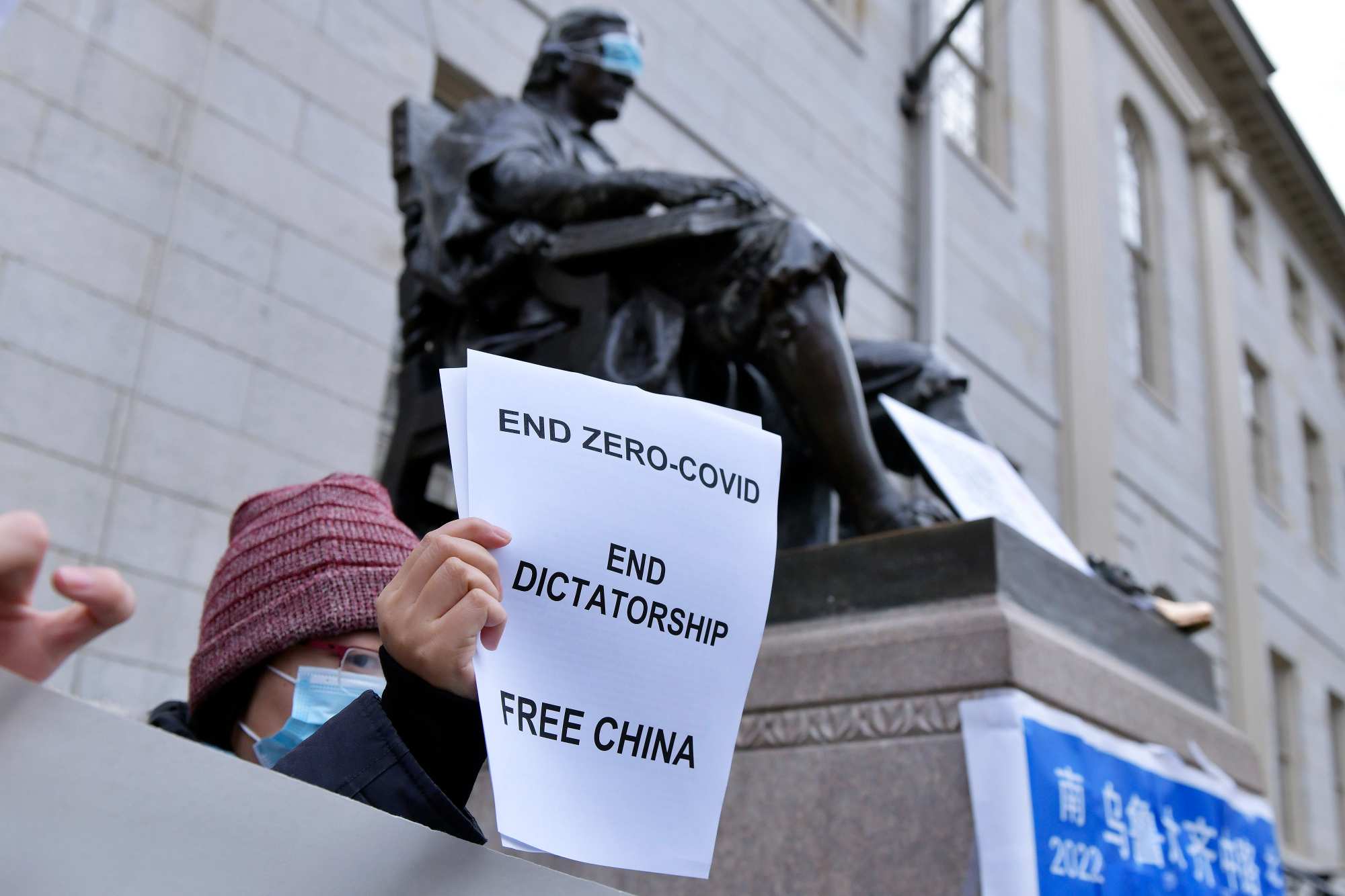 Demonstrators work to put a mask over the eyes of the John Harvard Statue in Harvard Yard as dozens of students and faculty demonstrated against strict anti-virus measures in China on Tuesday. (Josh Reynolds/AP)