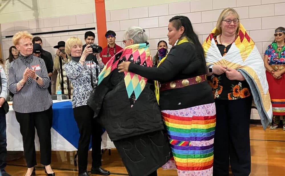 A member of the Oglala Lakota Nation wraps Liz Martin of the Barre Museum Association Board in a handmade quilt. Each of the museum board members received a quilt as a gift from the tribe. To the left are board members Maureen Marshall and Lucy Allen. To the right is Ann Meilus.(Nancy Eve Cohen/NEPM)