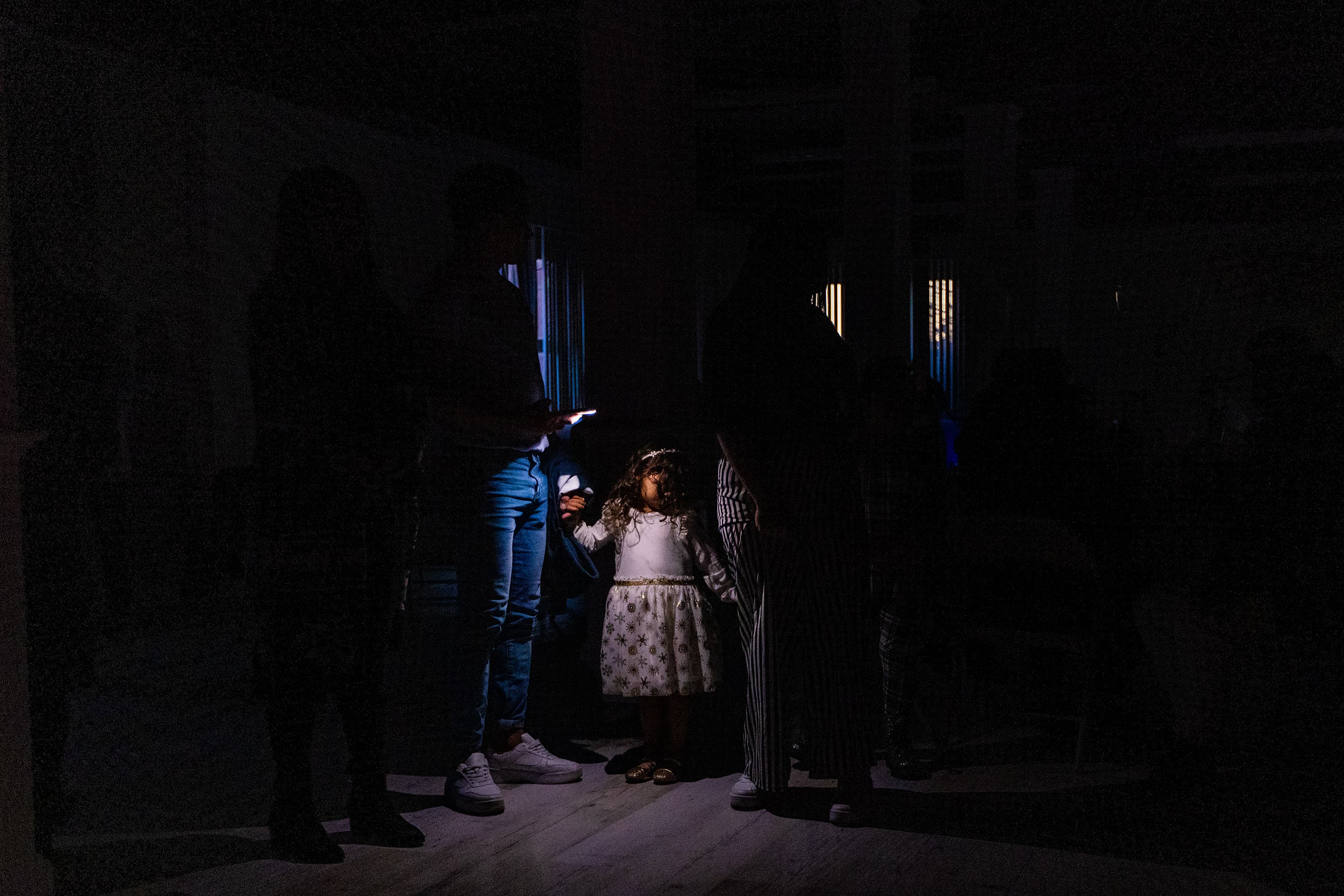Illuminated by a flashlight, 3-year-old Adalay Ramos and her family wait silently to surprise Isabel Rodriguez's mother with with a birthday celebration. (Jesse Costa/WBUR)