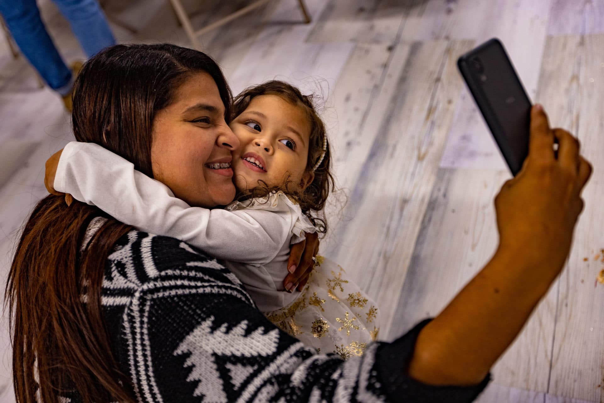 Adalay Ramos, 3, embraces her mother and takes a selfie at the party. (Jesse Costa/WBUR)